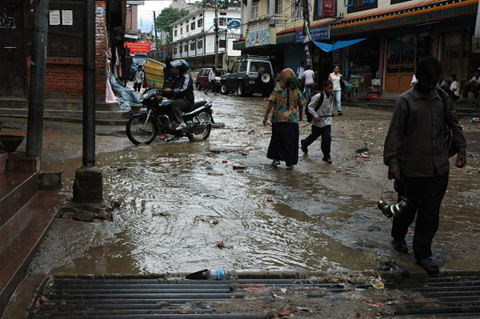 Rain runoff is chaneled into the sewer muddy day, people step gingerly in open shoes, even the motorcycle riders drive carefully, _Boudha_streets, Kathmandu, Nepal