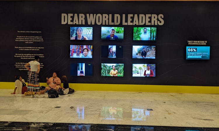 People sitting on floor of COP27 next to Dear World Leaders sign